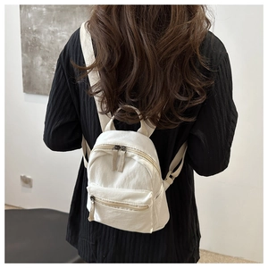 Rear view of a model wearing a mini cream canvas backpack with dual zipper compartments