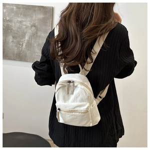 Rear view of a model wearing a white canvas mini backpack with adjustable straps