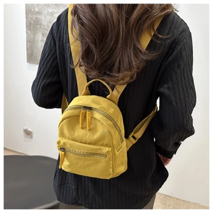 Rear view of model wearing a bright yellow mini backpack with waterproof nylon texture