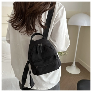 Minimalist black nylon mini backpack worn by model in a bright, modern interior setting