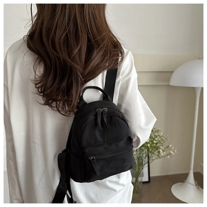 Detailed back view of a minimalist black mini nylon backpack worn by a model in a room