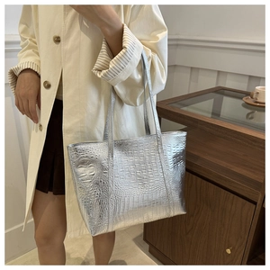 Close-up of silver tote bag with crocodile texture carried by a model in a trench coat