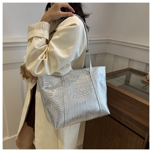 Silver metallic tote bag with crocodile embossed texture worn over a white trench coat