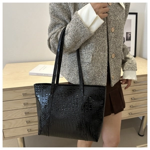 Detail of black crocodile texture tote bag with glossy finish on shoulder of a model