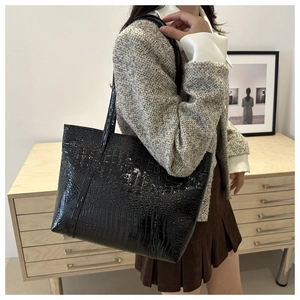 Close-up of black glossy faux crocodile embossed tote bag worn over the shoulder