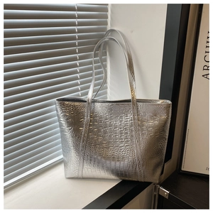 Detailed view of silver tote bag featuring a glossy crocodile pattern and long shoulder straps