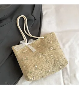 Détail du sac cabas en paille avec broderies florales, anse en corde et nœud dentelle