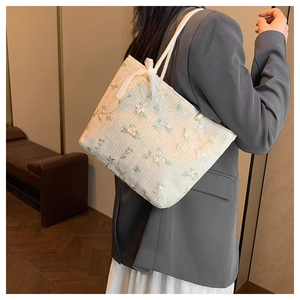 Détail d'un sac cabas tissé avec broderie florale et nœud porté à l'épaule