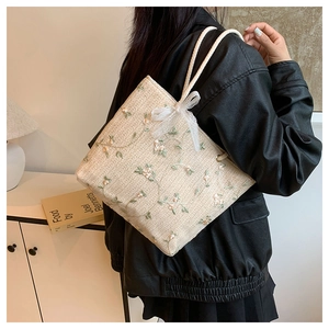 Détail du sac cabas en paille tressée avec broderie florale et nœud en dentelle blanche