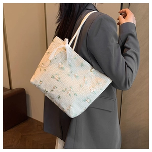 Vue détaillée du sac cabas beige tissé avec broderie florale et nœud en dentelle blanche
