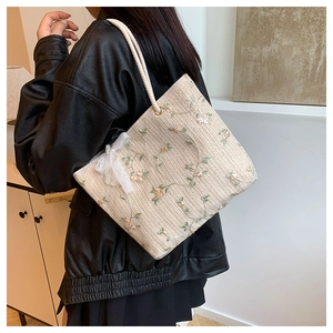 Détail du sac cabas beige tissé avec broderie florale et nœud en dentelle blanche