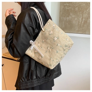 Détail du sac cabas en paille tissée beige avec broderie florale et nœud en dentelle
