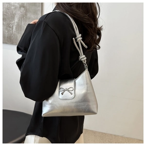Détail du sac seau métallisé argenté avec bandoulière nouée et nœud porté par le modèle