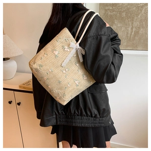 Détail d'un sac cabas en paille tissée avec broderie florale et nœud en dentelle blanche