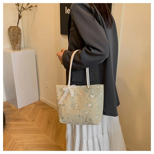 Détail de la broderie florale et du nœud en dentelle sur le sac cabas en paille d'été