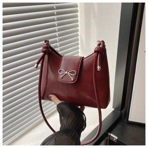 Détail du sac en cuir verni bordeaux avec boucle nœud argentée et bandoulière nouée