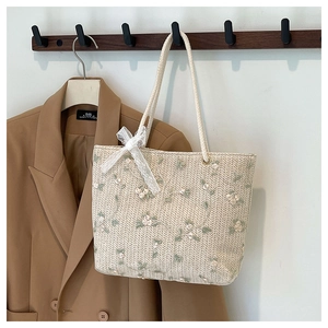 Détail du sac cabas en paille tressée avec broderie florale et nœud en dentelle