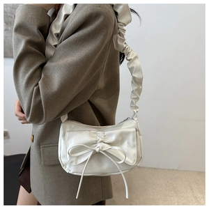 Close-up of a white patent leather shoulder bag with bow knot and scrunchie strap detail