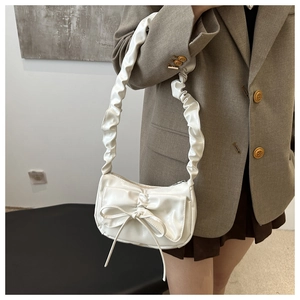 Close-up of white glossy leather shoulder bag featuring a large bow and ruffled strap