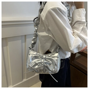 Detail view of a silver metallic bow bag with ruffled shoulder straps on a model