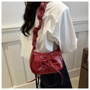 Detail of red bow crescent bag featuring glossy finish and ruffled shoulder strap