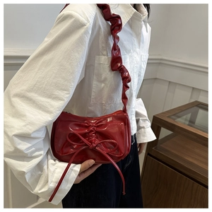 Detail of dark red patent leather crescent bag with bow decoration and pleated shoulder strap
