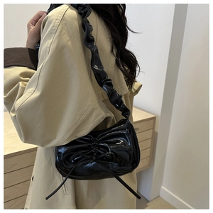 Detail of black patent leather hobo bag with ruffle shoulder strap and bow accent
