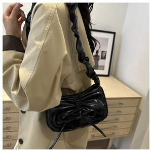 Detail of black glossy bow shoulder bag with pleated straps on model with trench coat