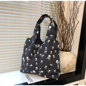 Detail van de zwarte tote bag met witte schedelpatronen tegen een minimalistische wand