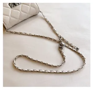 Detail of white quilted crossbody bag featuring silver chain strap and adjustable metal ball