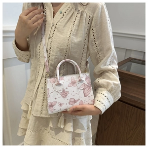 Detailed view of a white rectangular handbag with pink butterfly prints and a shoulder strap