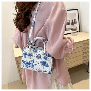 Detailed view of white crossbody bag with blue butterfly prints on an adjustable strap