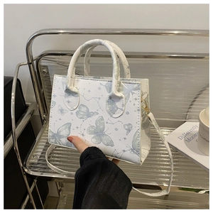 Détail du sac fourre-tout carré blanc avec imprimé papillon et finitions métalliques dorées