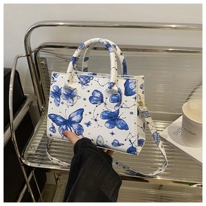Détail de la texture cuir blanc croisé avec motifs de papillons et d'étoiles bleus sur le sac