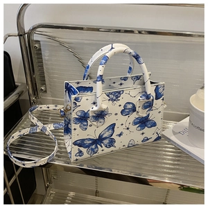 Détail du sac bandoulière blanc avec imprimé papillon bleu sur une étagère en métal