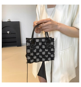 Detail of black and grey checkered tweed tote bag with frayed edges and leather handles