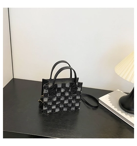 Detail view of a black and white checkerboard tweed crossbody bag with frayed edges and handles