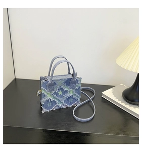 Detail of blue denim patchwork small square bag with frayed star patterns and top handle
