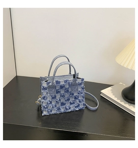 Detail of blue and white checkered denim tote bag with frayed edges and gold hardware hooks