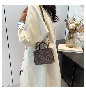 Dettaglio mini borsa in pelle marrone con motivo a M su sfondo di un trench beige chic