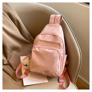 Détail d'un sac bandoulière en nylon rose avec plusieurs poches et pendentif ours en peluche