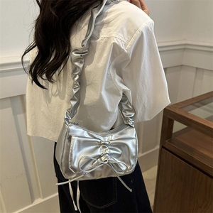 Silver metallic shoulder bag with ruffled strap and large bow detail shown on a model