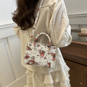 Vintage white crossbody bag with butterfly prints and top handle on a wooden cabinet