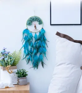 Detail of Tree of Life dream catcher with green stones and teal feathers on a white wall