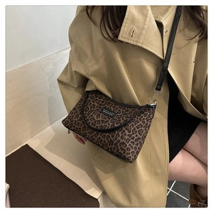 Detail of leopard print handbag featuring a black leather strap and brand logo patch