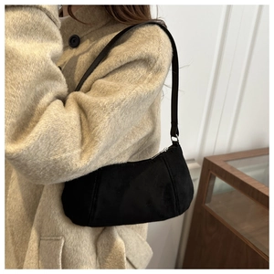 Détail d'un sac sous le bras en daim noir porté avec un manteau en laine élégant