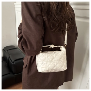 Detail of white quilted heart pattern shoulder bag worn with brown coat for daily style