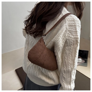 Gros plan d'un sac demi-lune en daim marron foncé mat porté avec un pull en maille blanche