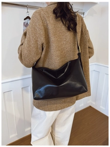 Model wearing a large black soft leather crossbody bag with pleated slouchy style design