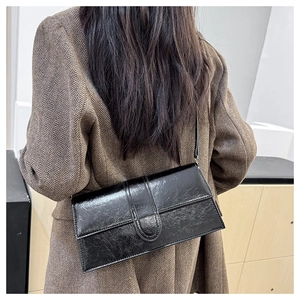 Detail of black glossy textured leather baguette shoulder bag on a female model